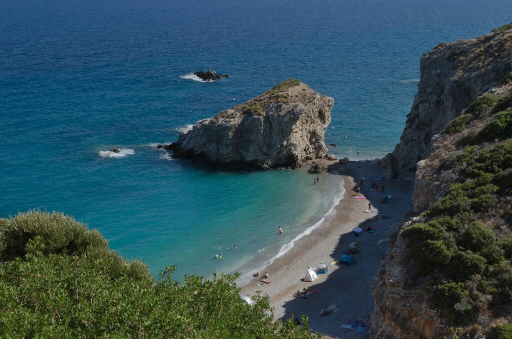 Scenic beach cove in Kythira, Greece, with clear blue water, sandy shoreline, and lush greenery.