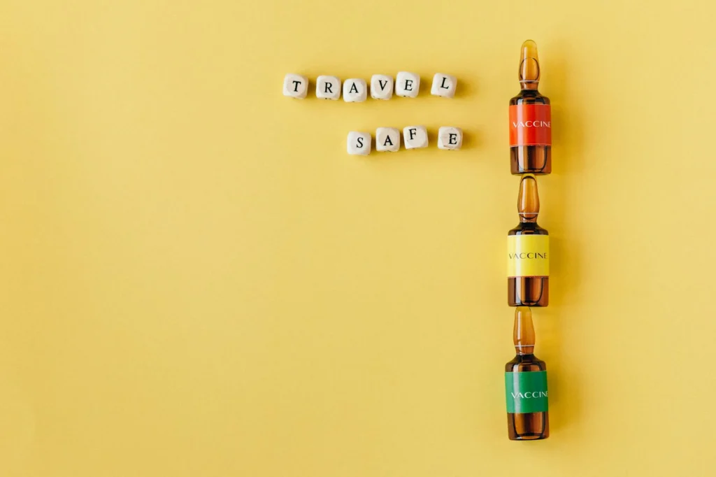 Three vaccine vials with a 'Travel Safe' message arranged on a yellow background, conveying safety and health themes.