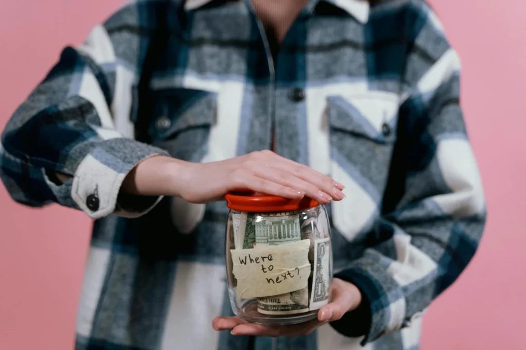 Woman in plaid shirt holds money jar with travel goals in mind.