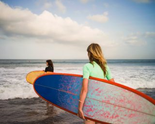 Two woman walking out to sea, carrying surfboards, Seminyak, Bali, Indonesia